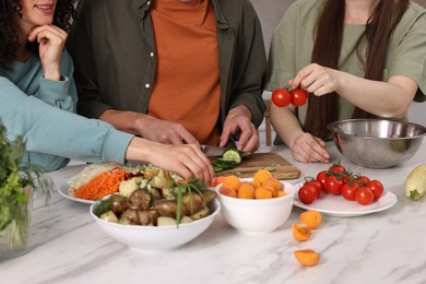 Photo of Friends cooking healthy vegetarian meal at white marble table in kitchen, closeup