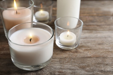 Burning wax candles in glasses on wooden table