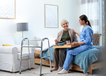 Care worker serving dinner for elderly woman in geriatric hospice
