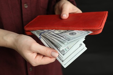 Money exchange. Woman putting dollar banknotes into wallet on dark background, closeup