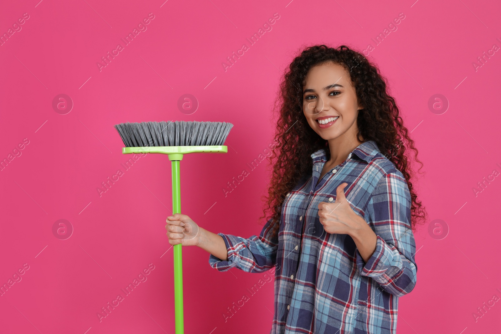 Photo of African American woman with green broom on pink background