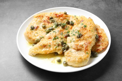 Photo of Delicious chicken piccata with herbs on grey table, closeup