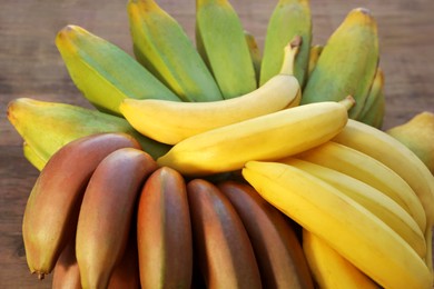 Photo of Different sorts of bananas on wooden table, closeup