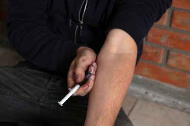 Photo of Male drug addict making injection near brick wall, closeup of hands