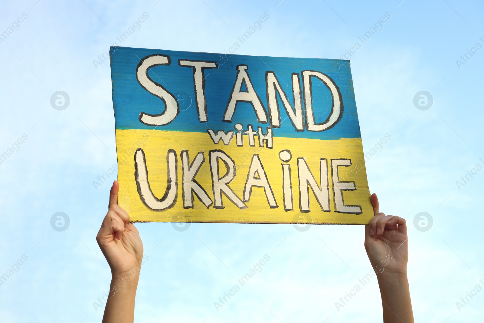 Photo of Woman holding poster Stand with Ukraine against blue sky, closeup