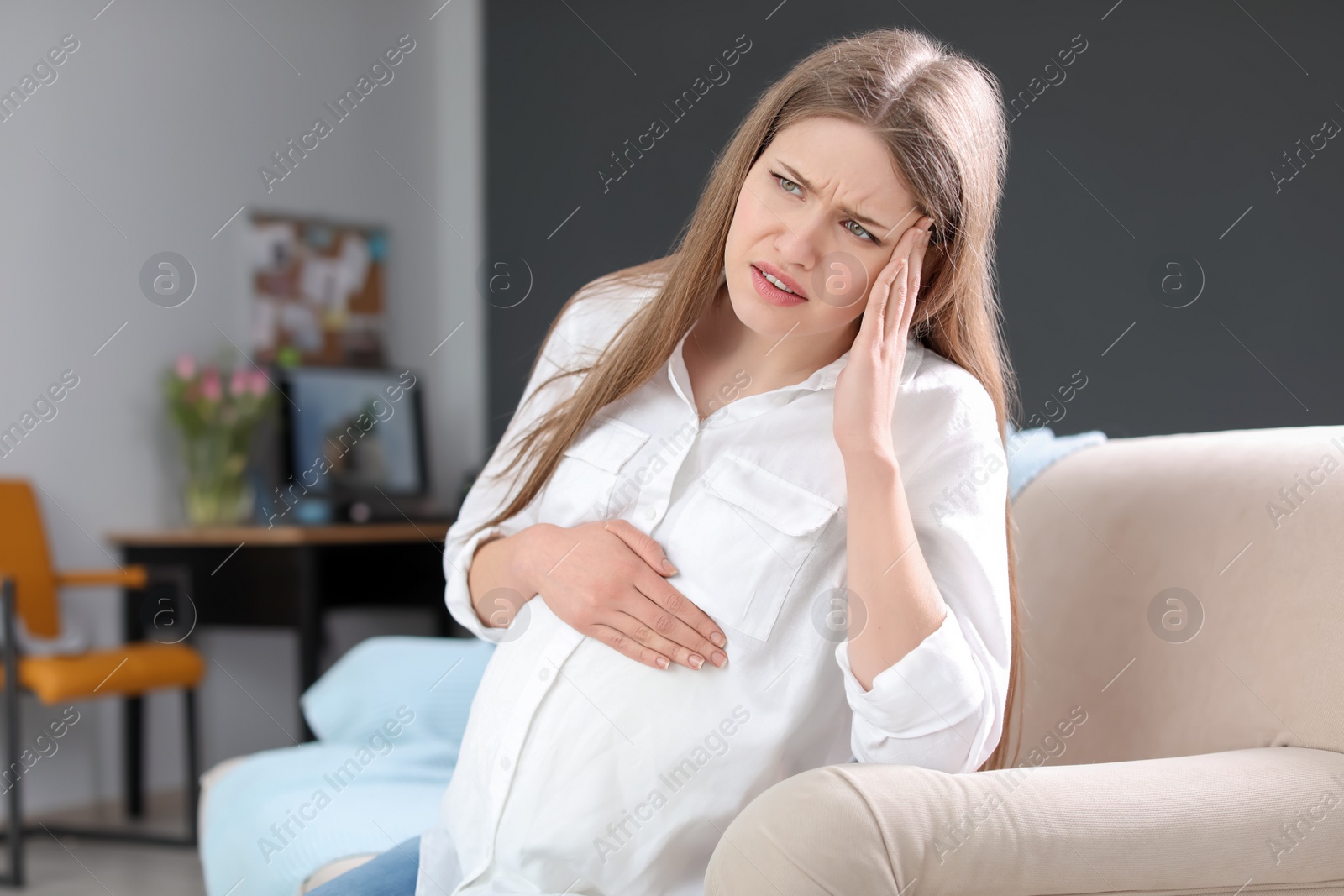 Photo of Young pregnant woman suffering from headache at home