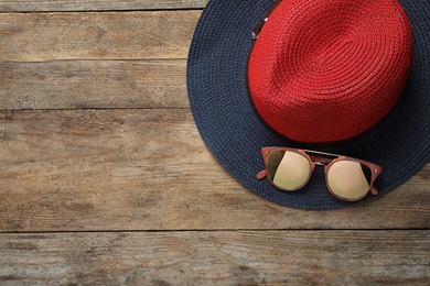 Hat with sunglasses and space for text on wooden background, flat lay. Beach accessories