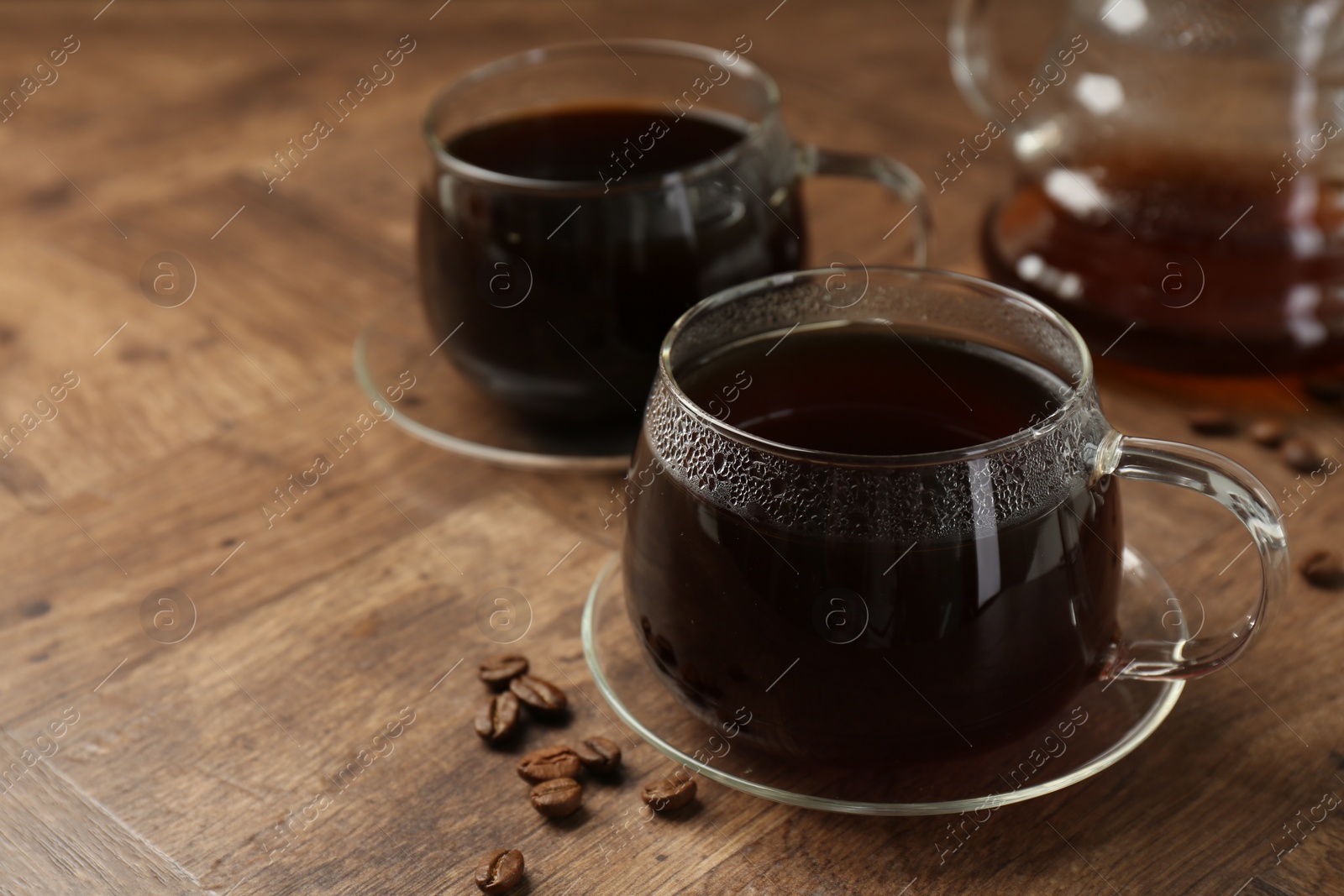 Photo of Hot coffee in glass cups and beans on wooden table, closeup. Space for text