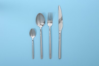 Stylish silver cutlery set on light blue background, flat lay