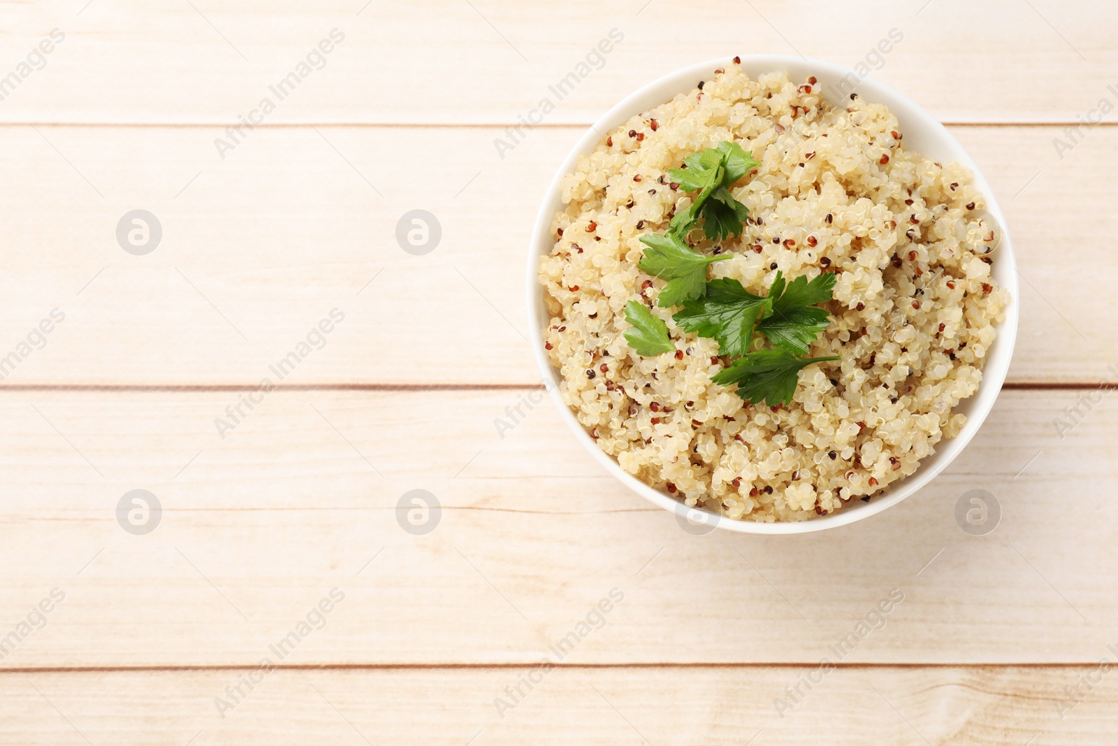 Photo of Tasty quinoa porridge with parsley in bowl on light wooden table, top view. Space for text