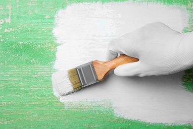 Person painting green wooden surface white, closeup