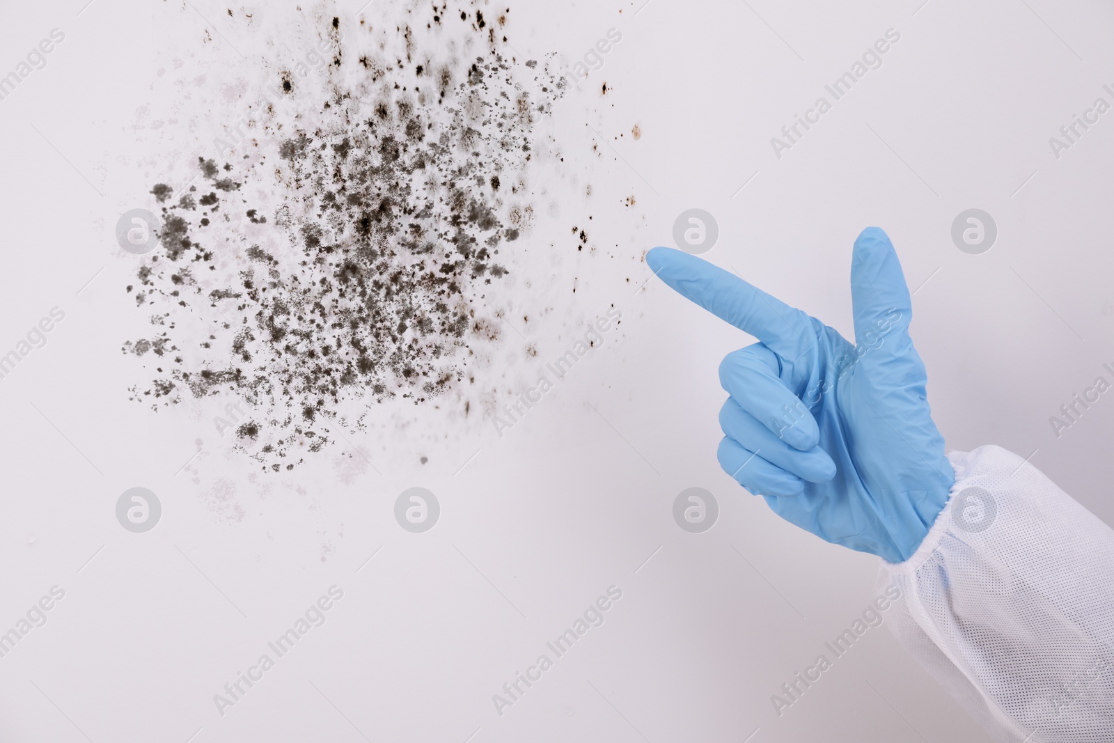 Image of Woman in protective suit pointing at wall affected with mold, closeup