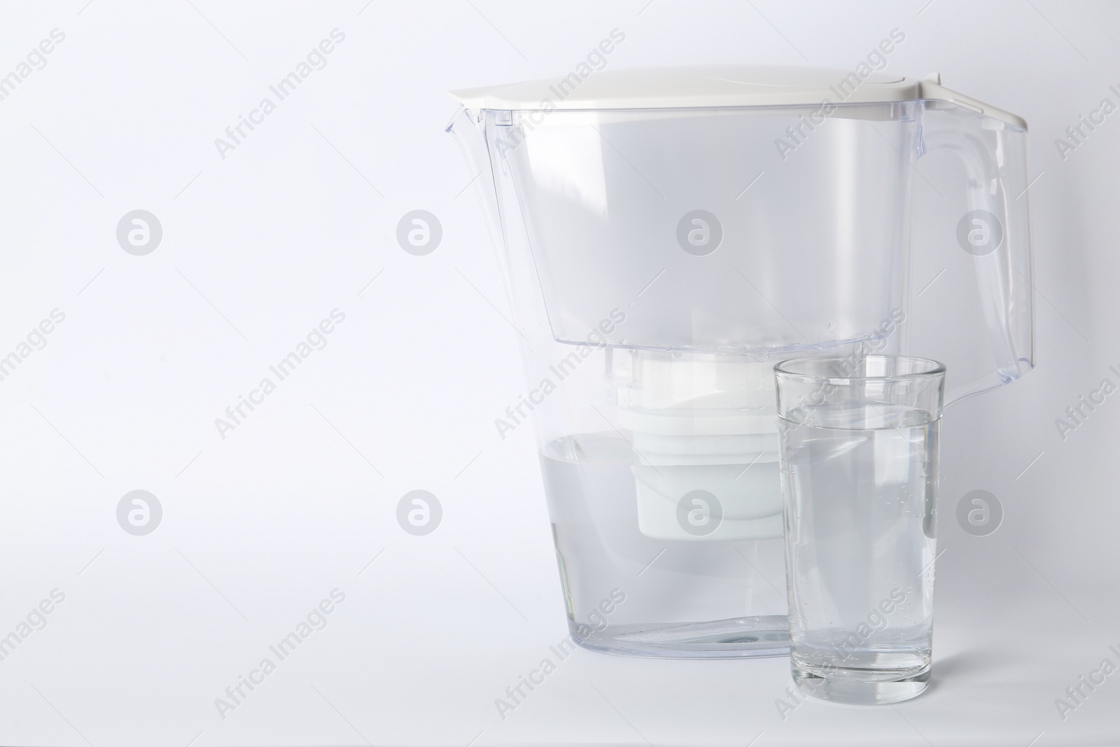 Photo of Filter jug and glass with purified water on white background. Space for text