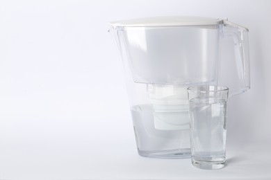 Photo of Filter jug and glass with purified water on white background. Space for text