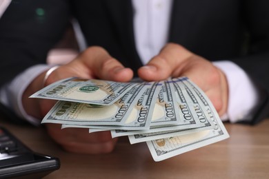 Money exchange. Man counting dollar banknotes at wooden table, closeup