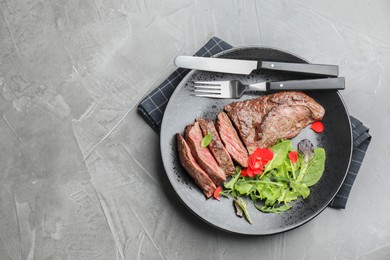 Photo of Delicious grilled beef meat served with greens on grey table, top view. Space for text