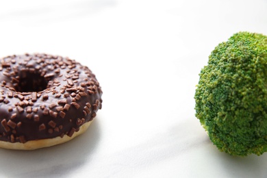 Photo of Concept of choice between healthy and junk food, closeup. Tasty doughnut with broccoli on white table