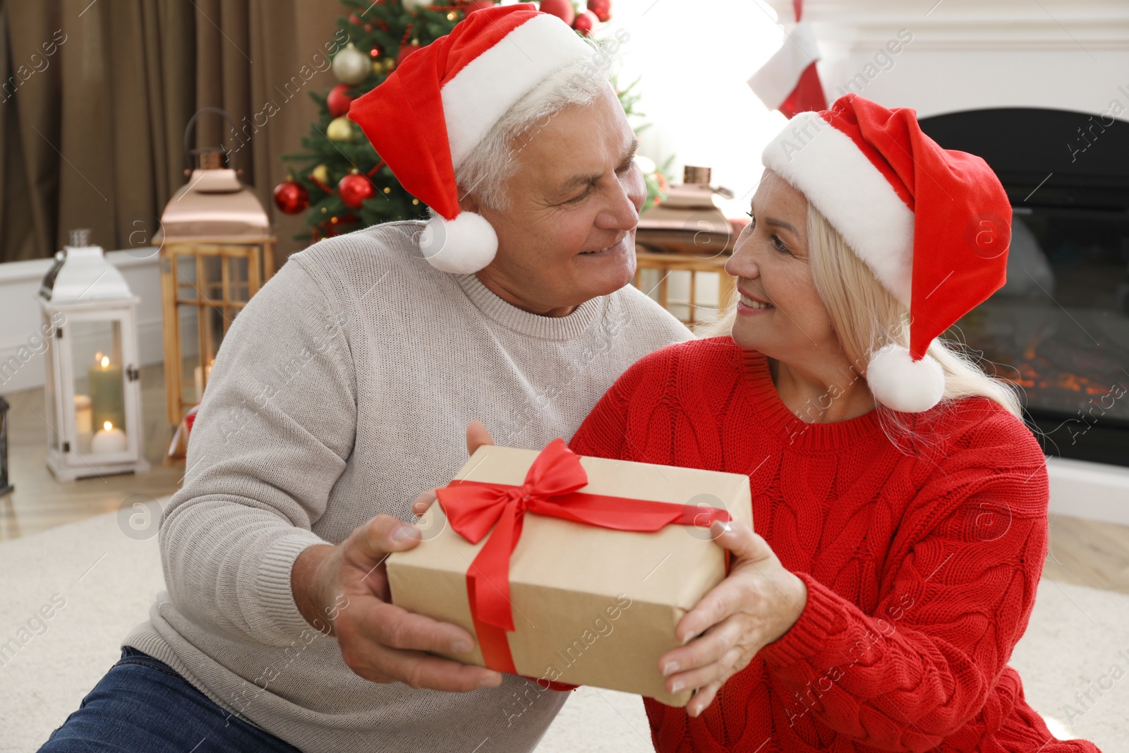 Photo of Happy mature couple in Santa hats with gift box at home. Christmas celebration