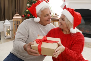 Photo of Happy mature couple in Santa hats with gift box at home. Christmas celebration