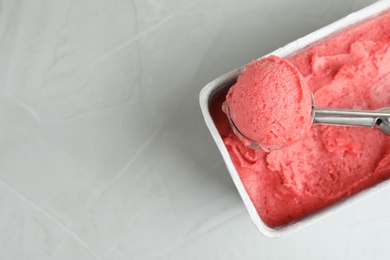 Photo of Container with delicious pink ice cream and scoop on grey table, top view. Space for text