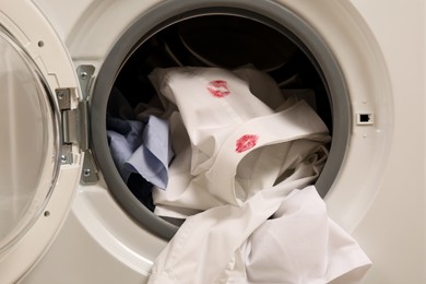 Photo of Men's shirt with lipstick kiss marks among other clothes in washing machine, closeup