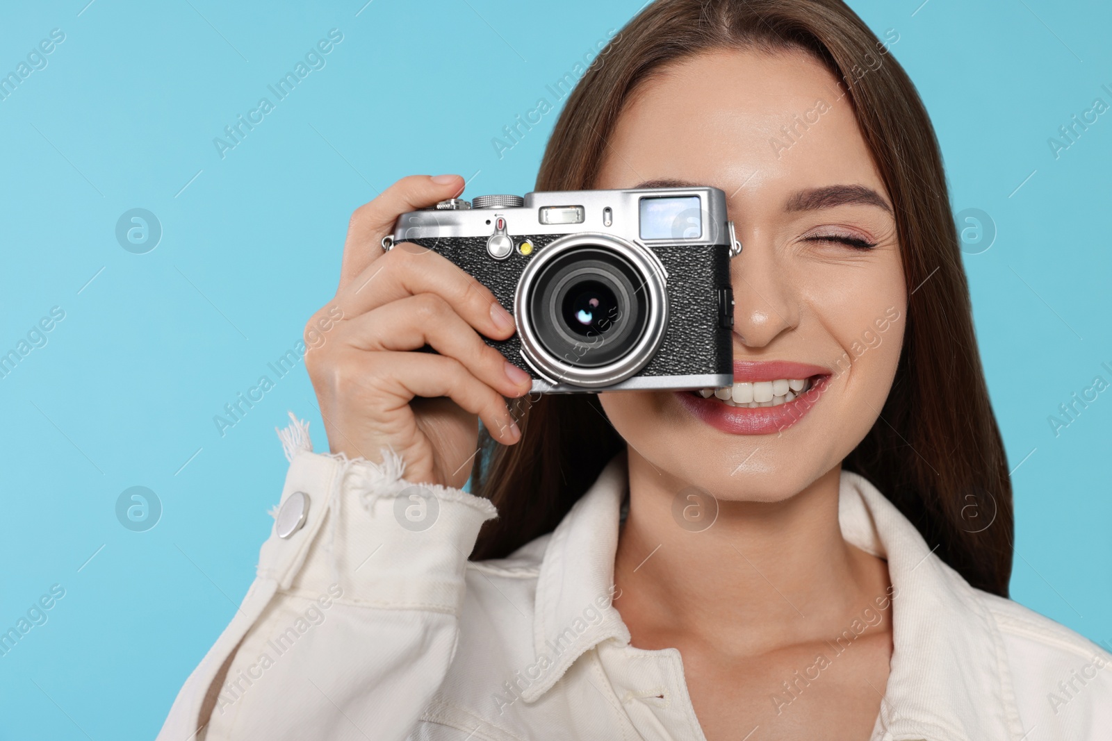 Photo of Young woman with camera taking photo on light blue background. Interesting hobby