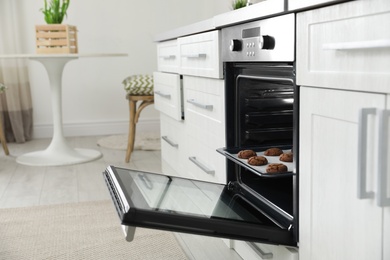 Open modern oven with tray of baked cookies in kitchen