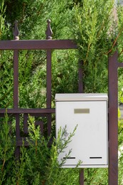 Photo of White metal letter box on fence near tree outdoors