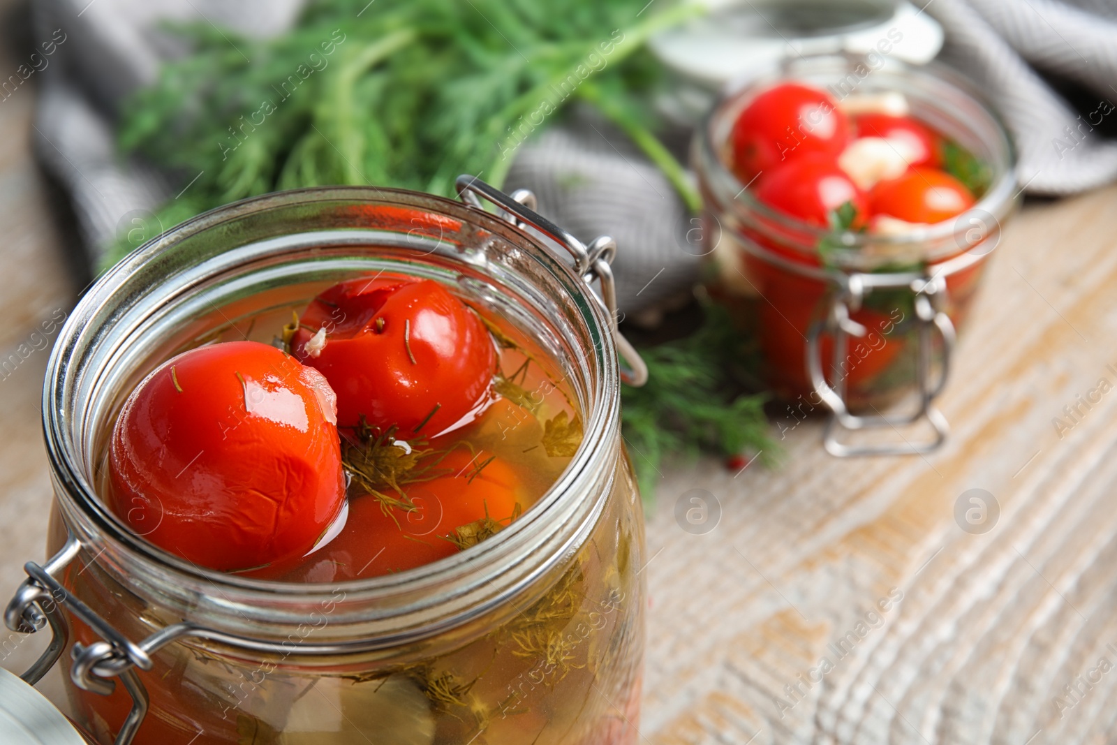 Photo of Pickled tomatoes in glass jars and products on wooden table, closeup view