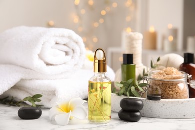 Photo of Beautiful spa composition with essential oil and plumeria flower on white marble table against blurred lights
