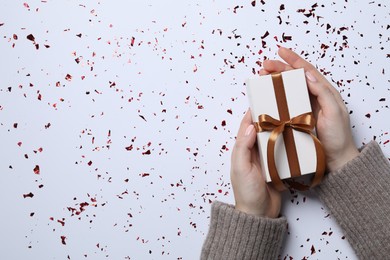 Photo of Christmas present. Woman with gift box and confetti on white background, top view. Space for text
