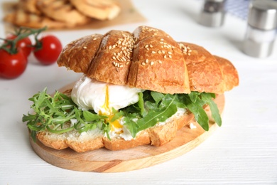 Delicious croissant with arugula and egg on white wooden table, closeup