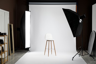 Photo of White photo background, chair and professional lighting equipment in studio