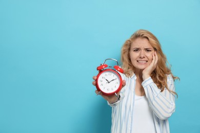 Emotional woman with alarm clock in turmoil over being late on light blue background. Space for text