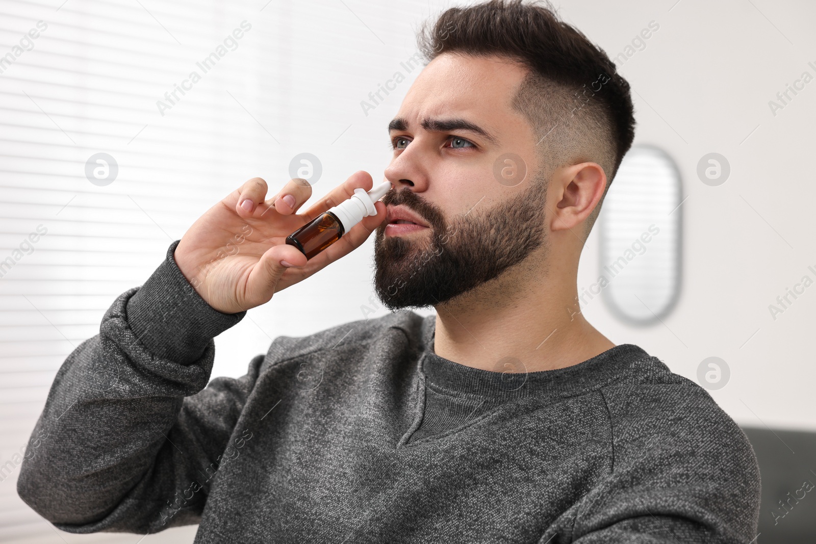 Photo of Medical drops. Young man using nasal spray indoors