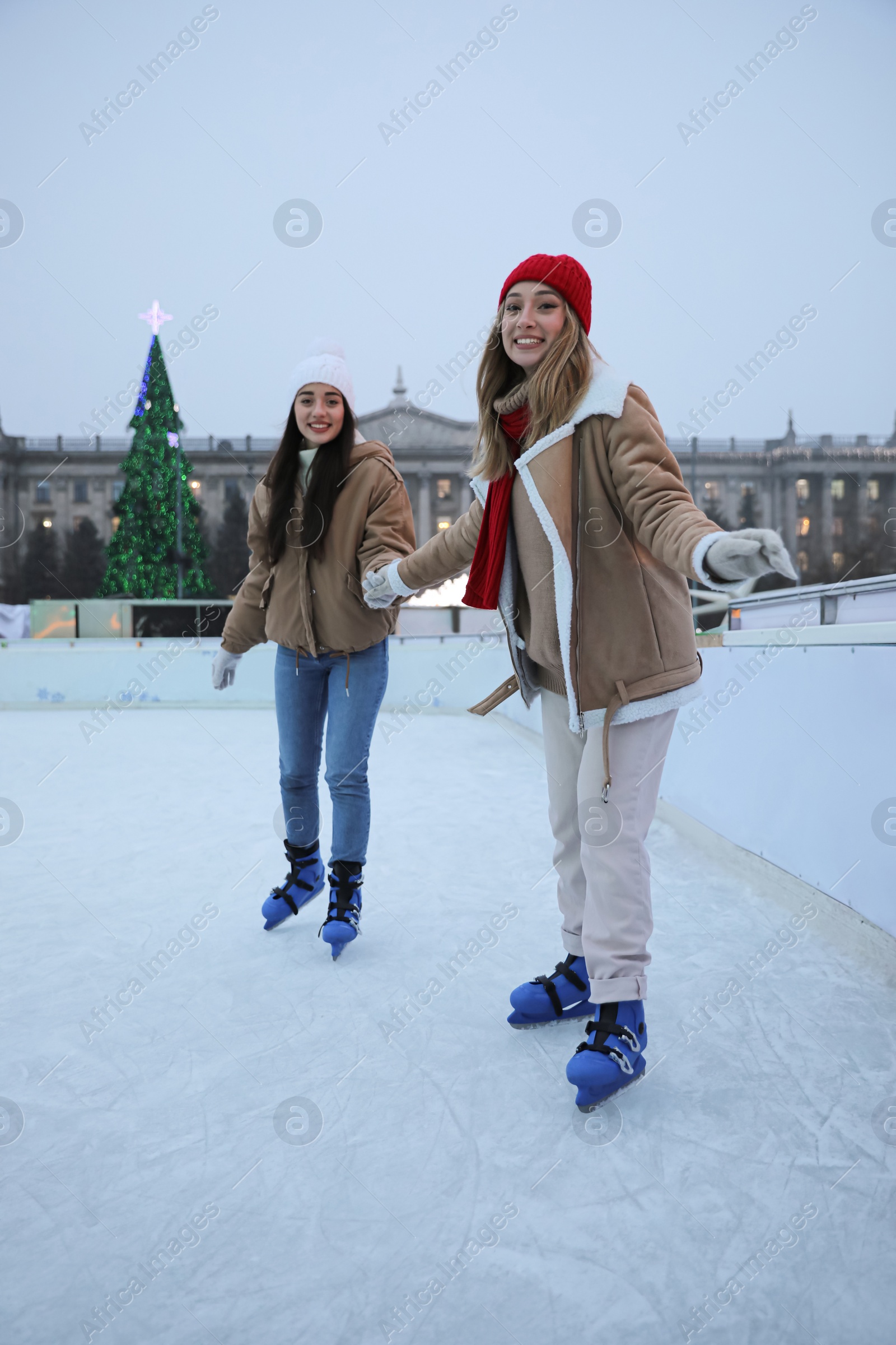 Image of Happy young women skating at outdoor ice rink