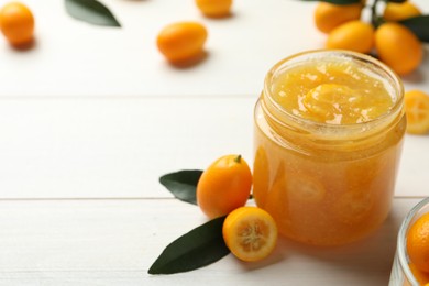 Delicious kumquat jam in jar and fresh fruits on white wooden table, space for text