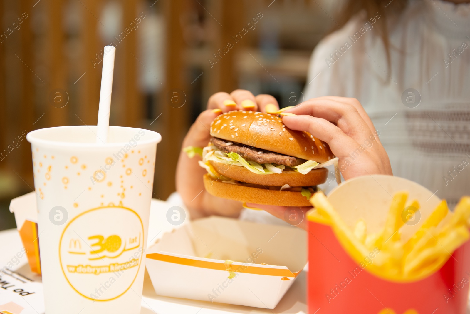 Photo of WARSAW, POLAND - SEPTEMBER 04, 2022: Woman with McDonald's burger, French fries and drink at table in cafe, closeup