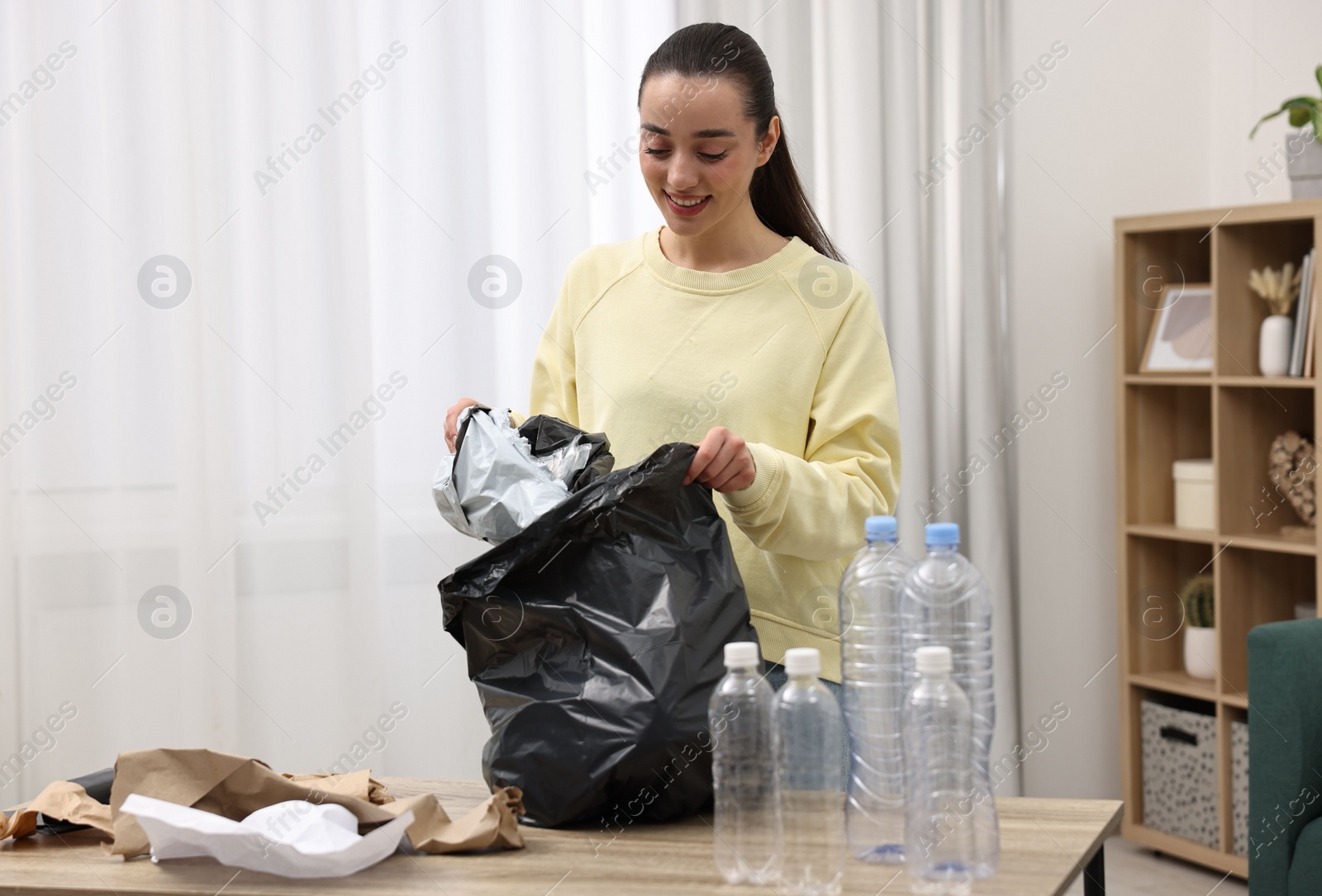 Photo of Smiling woman with plastic bag separating garbage in room