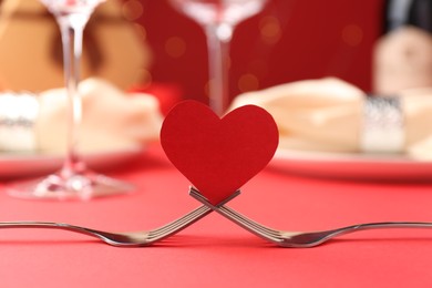 Photo of Joined forks with paper heart on red table, closeup. Romantic dinner