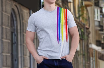 Image of Young man wearing t-shirt with image of LGBT pride flag outdoors