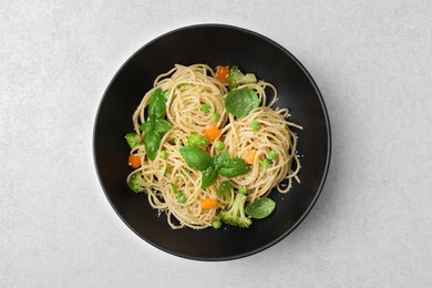 Delicious pasta primavera with basil, broccoli and peas on light grey table, top view