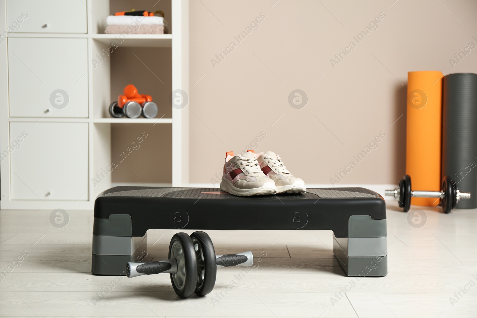 Photo of Step platform, sneakers and abdominal wheel indoors. Sports equipment