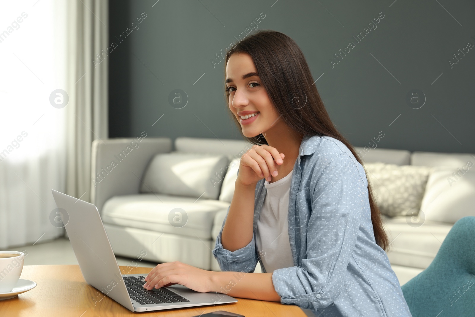 Photo of Young woman using laptop for search at wooden table in living room