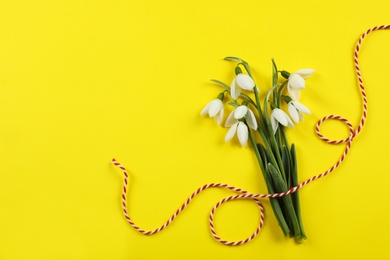 Photo of Beautiful snowdrops with traditional cord martisor on yellow background, flat lay and space for text. Symbol of first spring day