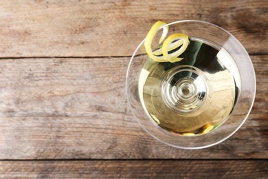 Photo of Glass of lemon drop martini cocktail with zest on wooden table, top view. Space for text