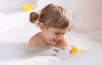 Photo of Smiling girl bathing with toy duck in tub