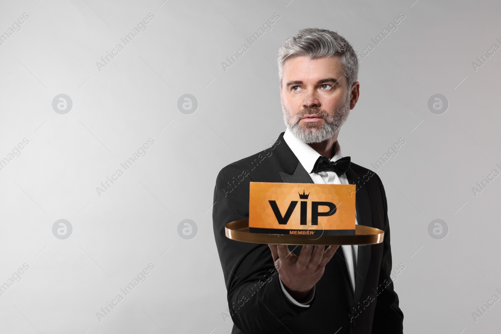 Photo of Handsome man holding tray with VIP sign on light grey background. Space for text