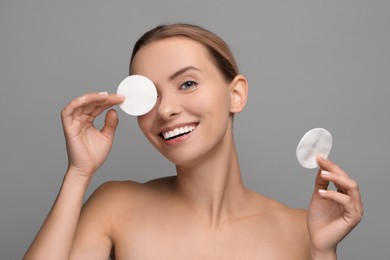 Smiling woman removing makeup with cotton pads on grey background