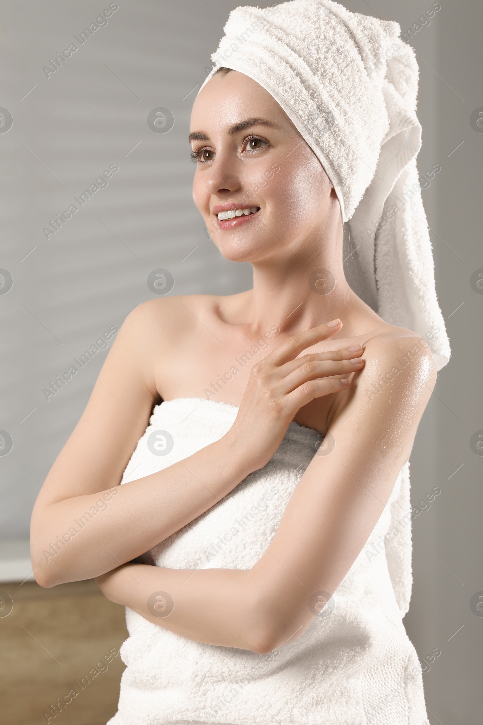 Photo of Happy woman applying body oil onto shoulder in bathroom